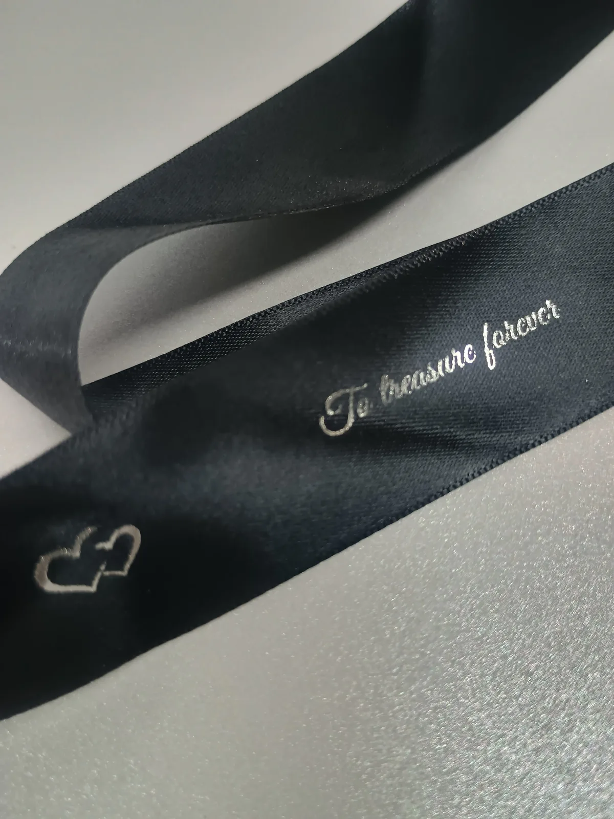 Black ribbon with silver-coloured lettering and linked-heart details